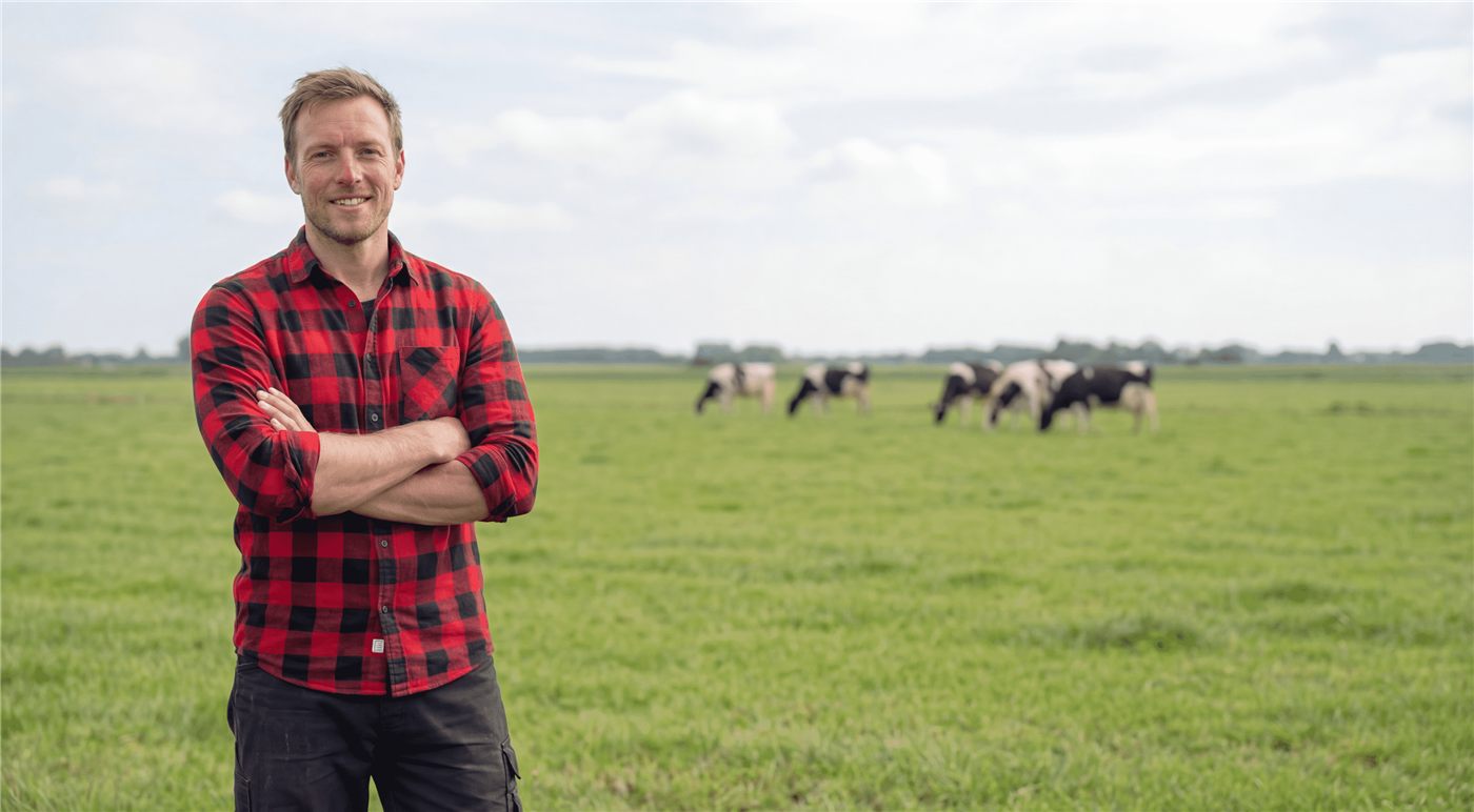 Een van de boeren van Kunstgrasboer in het weiland, met koeien op de achtergrond