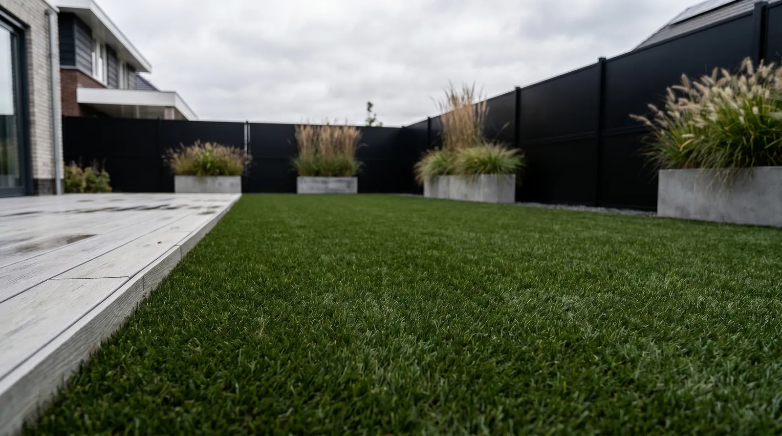 Strakke stadstuin met kunstgras, siergrassen en een houten terras